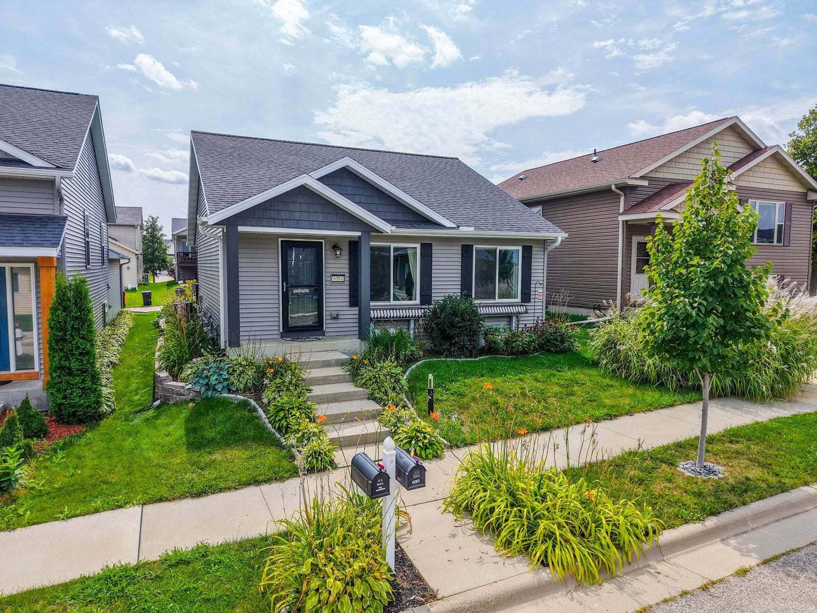 Front of 6084 Sandstone St NW with a covered porch, dark shutters and landscaped yard