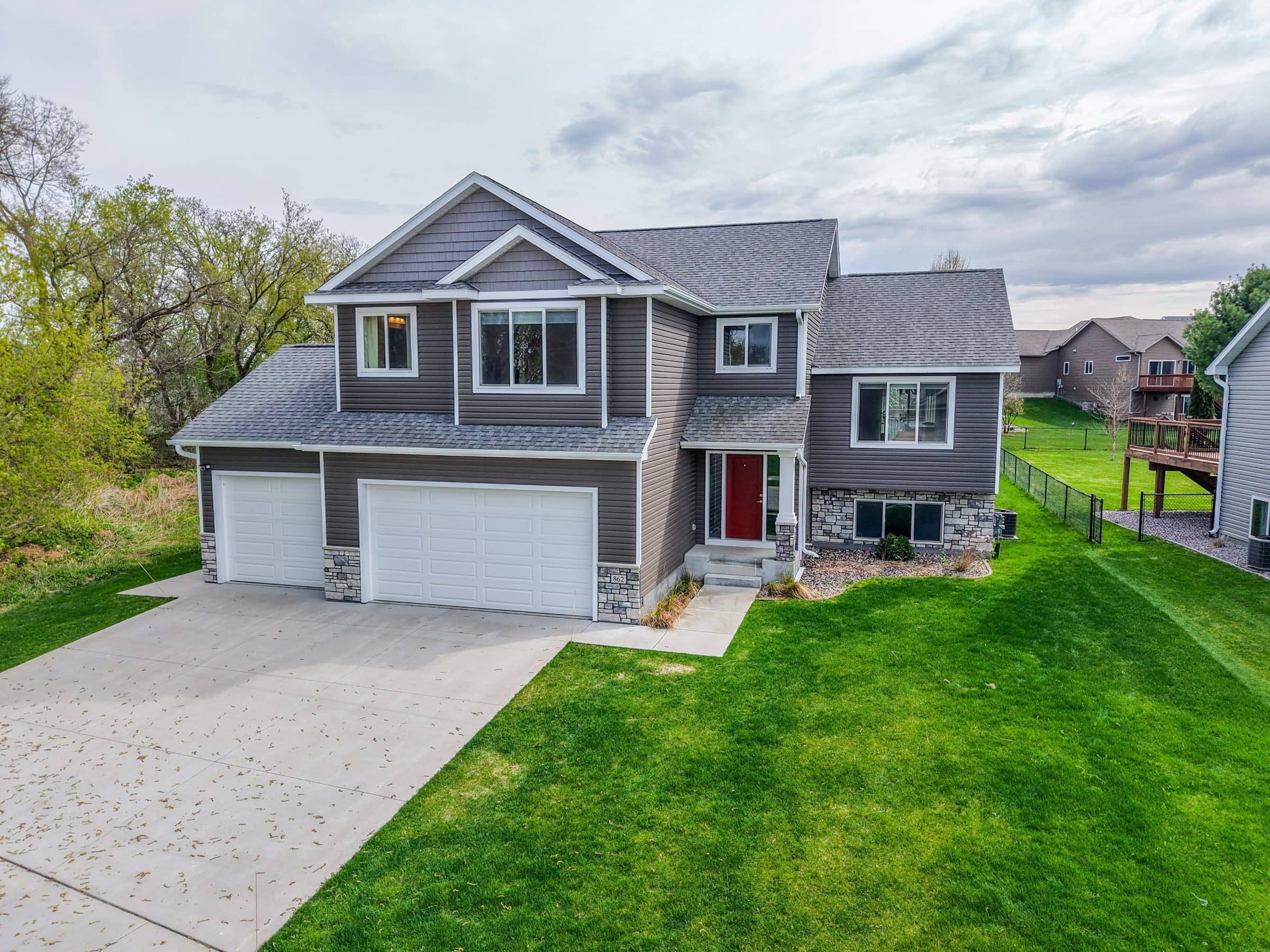 Two-story home with gray siding, a red front door and a three-car garage